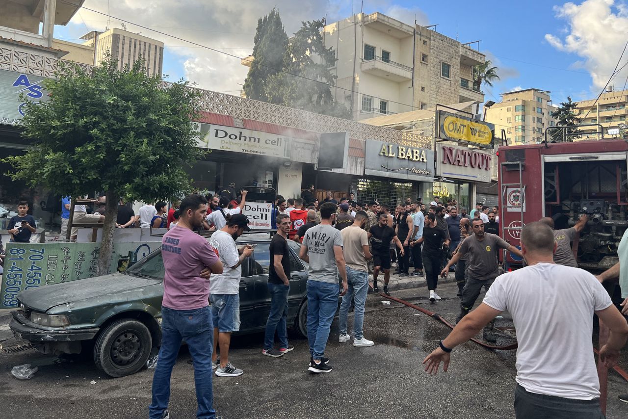 People gather as fire fighters put out the flames at the scene of a reported device explosion in Saida, Lebanon, on September 18.