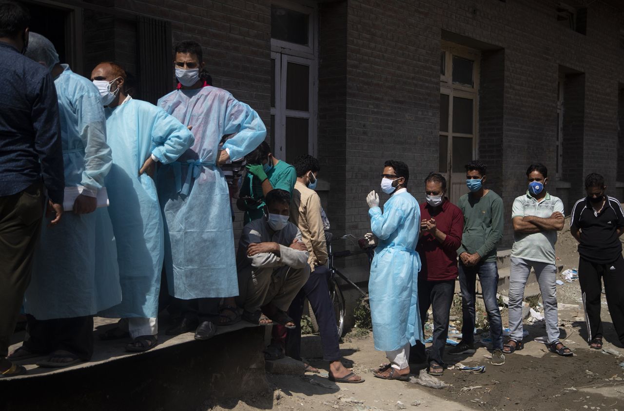 Relatives and bystanders, some of them wearing protective suits, line up to get oxygen cylinders for patients outside a hospital in Srinagar, Indian controlled Kashmir, on Wednesday, August 12. 