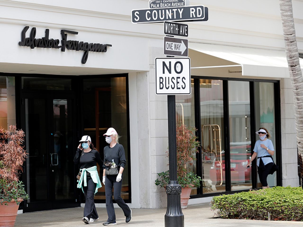 People wear protective face masks as they walk along Worth Ave. as shops began to reopen during the new coronavirus pandemic, Monday, May 11, in Palm Beach, Florida.