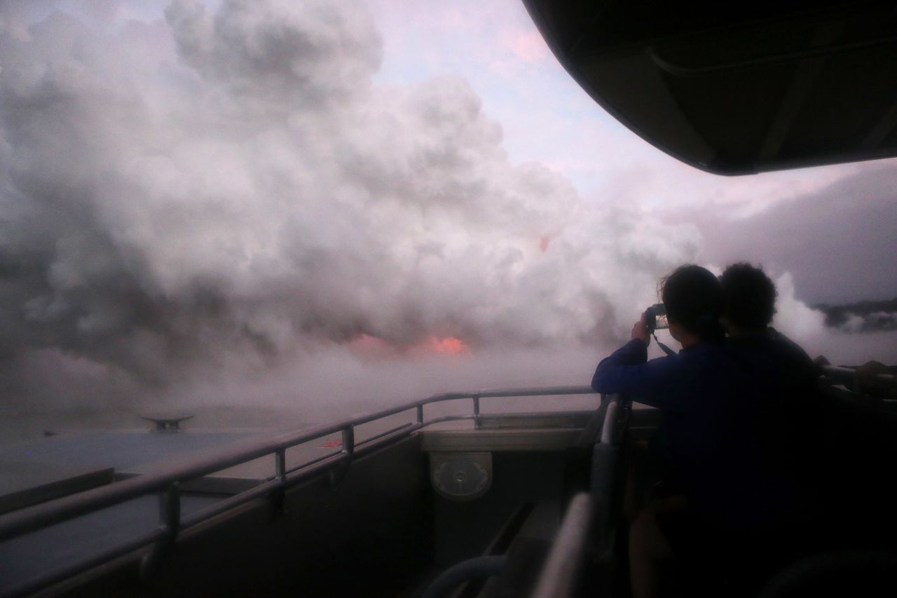 People ride a tour boat to view Kilauea volcano lava entering the Pacific Ocean at dawn, as a steam plume rises, on Hawaii's Big Island on May 22, 2018.