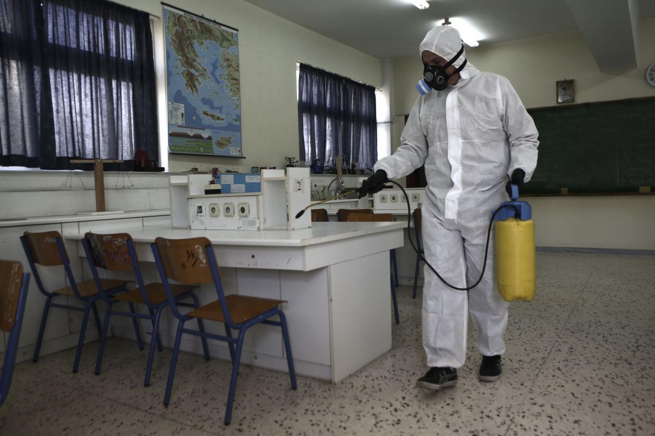 A worker wearing a protective suit sprays disinfectant inside a classroom at a high school in Athens, Greece on Friday, March 6.