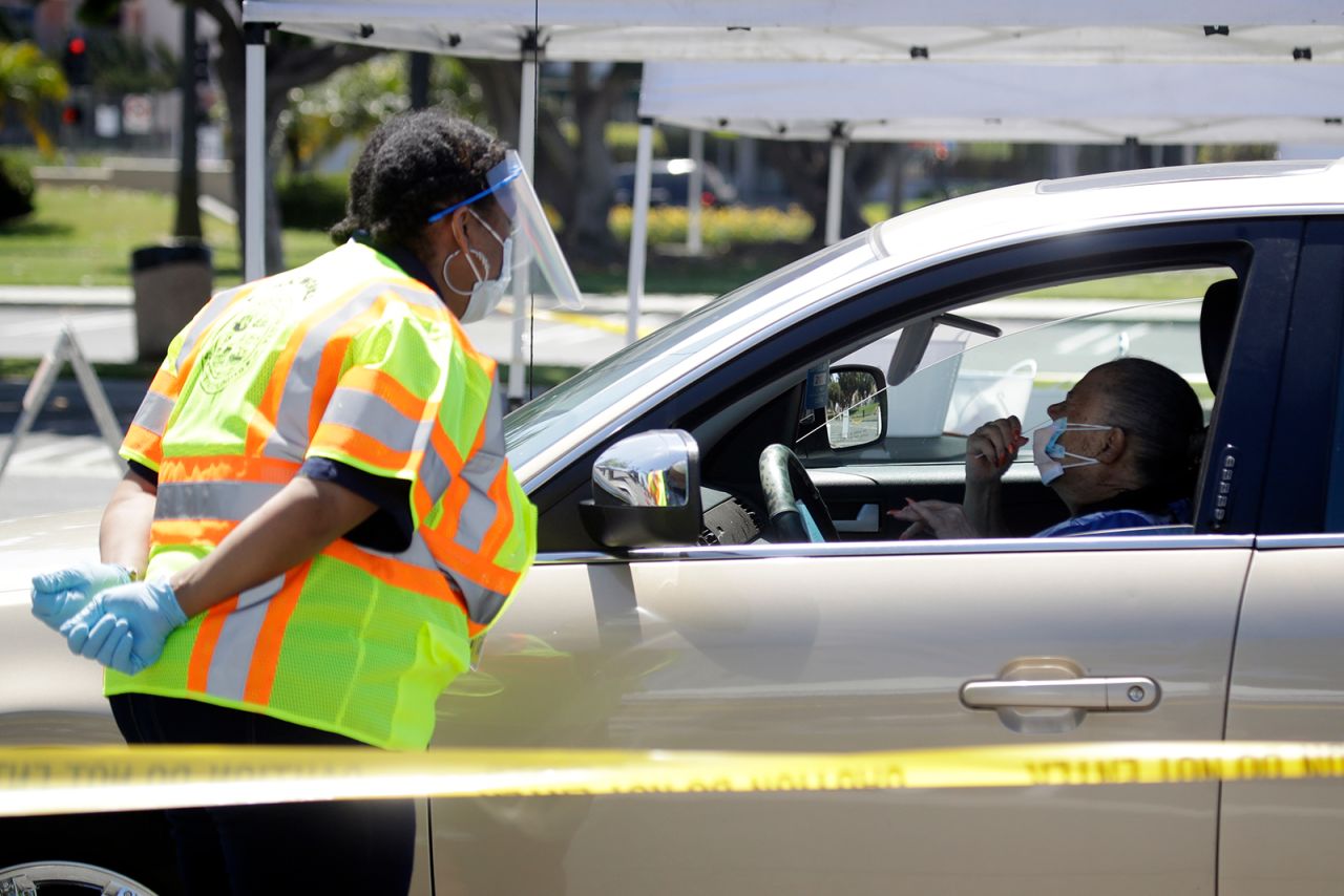 City worker Mickie Sanchez, left, helps a motorist with a drive-up Covid-19 test on April 27, in Carson, California.
