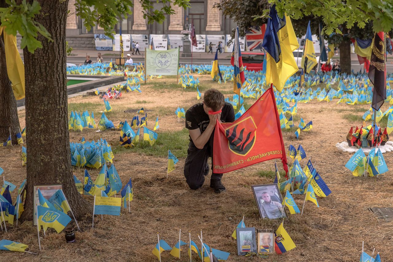 A man holding a flag of Ukrainian 55th Artillery Brigade kneels down at a memorial area with Ukrainian and other countries flags commemorating fallen Ukrainian and foreign fighters at the Independence Square, in Kyiv, on May 27.