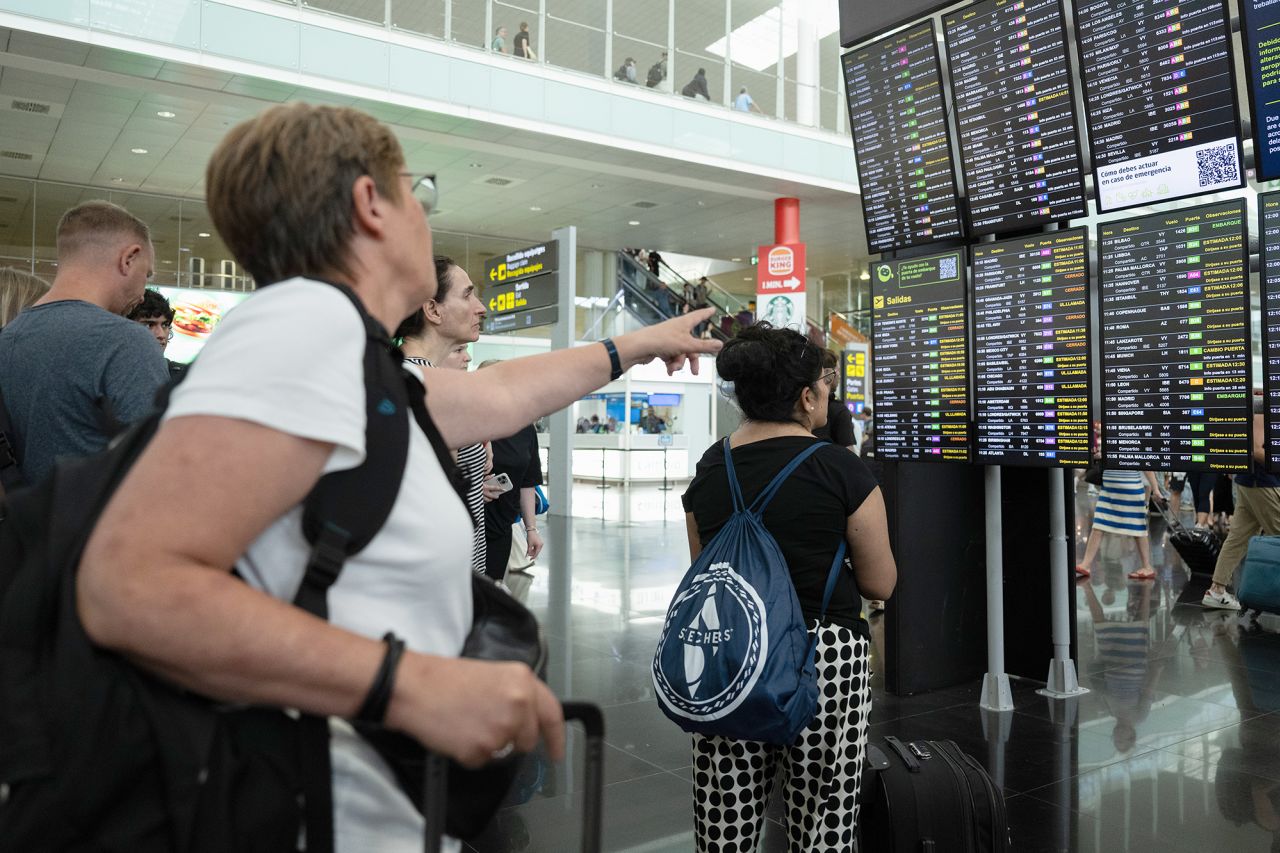 Passengers look at a screen displaying delayed flights at Barcelona Airport on July 19, in Barcelona, Spain. 