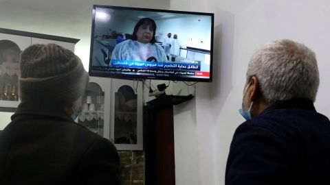Men in Hebron, West Bank, watch a live television broadcast as Palestinian Health Minister Mai Al-Kaila announces the start of Covid-19 vaccinations.