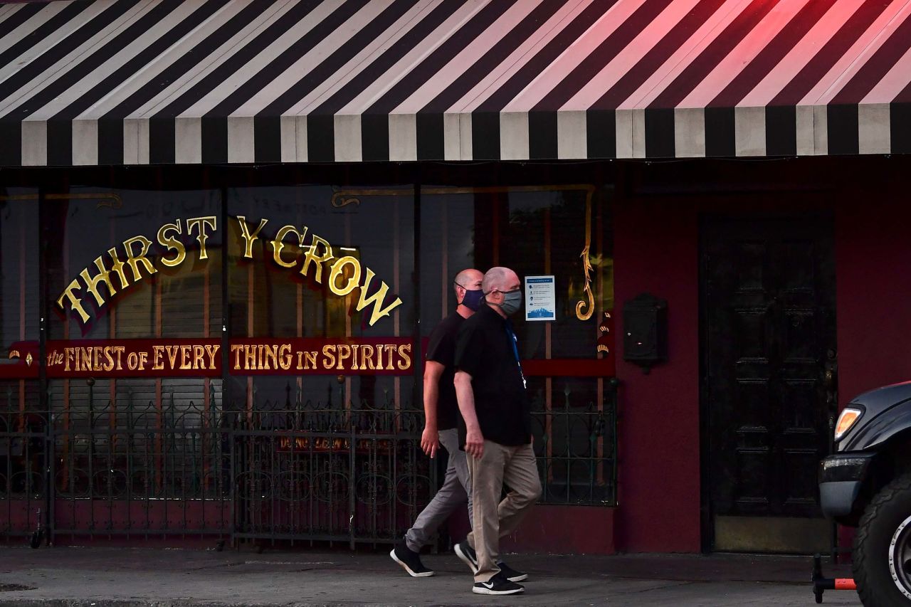 People wearing face masks walk past a closed bar in Los Angeles, California on June 29.