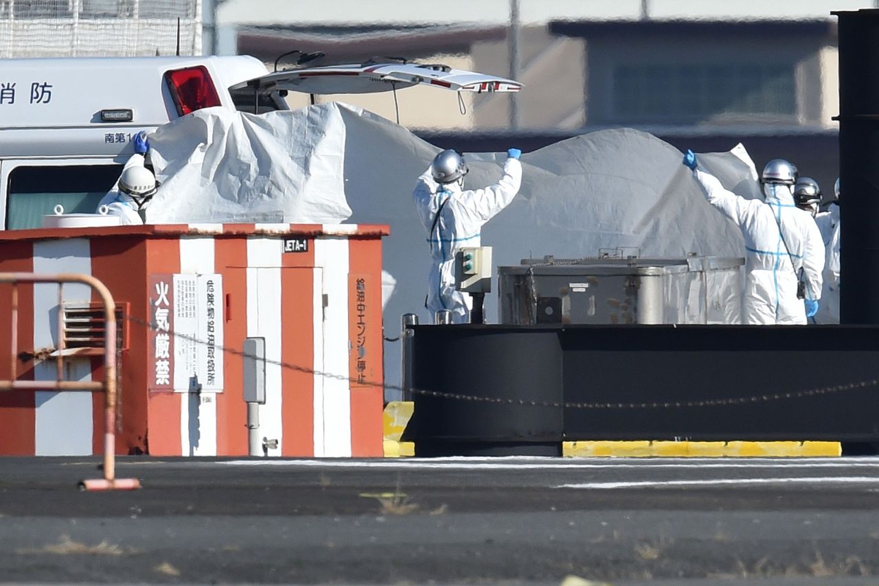 Workers in protective gear hold up a sheet as a passenger is transferred into a waiting ambulance at the Japan Coast Guard base in Yokohama on February 5 after being brought from the cruise ship Diamond Princess.