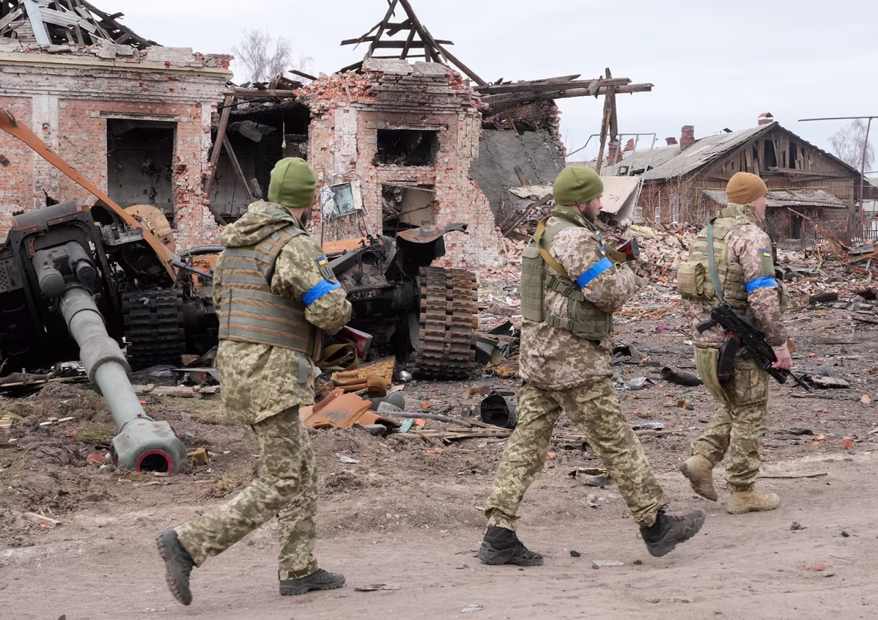 Ukrainian soldiers pass by a damaged Russian tank in the town of Trostyanets, east of Kyiv, on Monday. 