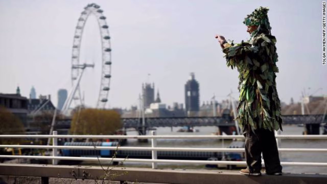A man dressed as a tree takes a photo of the protest on Waterloo Bridge, with the London Eye and Houses of Parliament in the backdrop. 