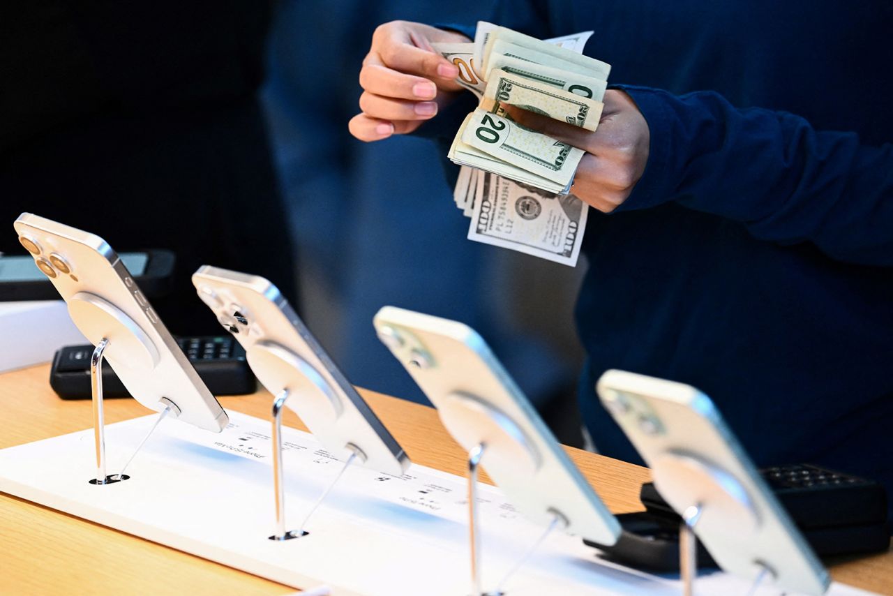 An employee counts US dollar currency as a customer pays cash for an Apple iPhone 15 series phone for sale at The Grove Apple retail store on release day in Los Angeles, California, on September 22, 2023. 