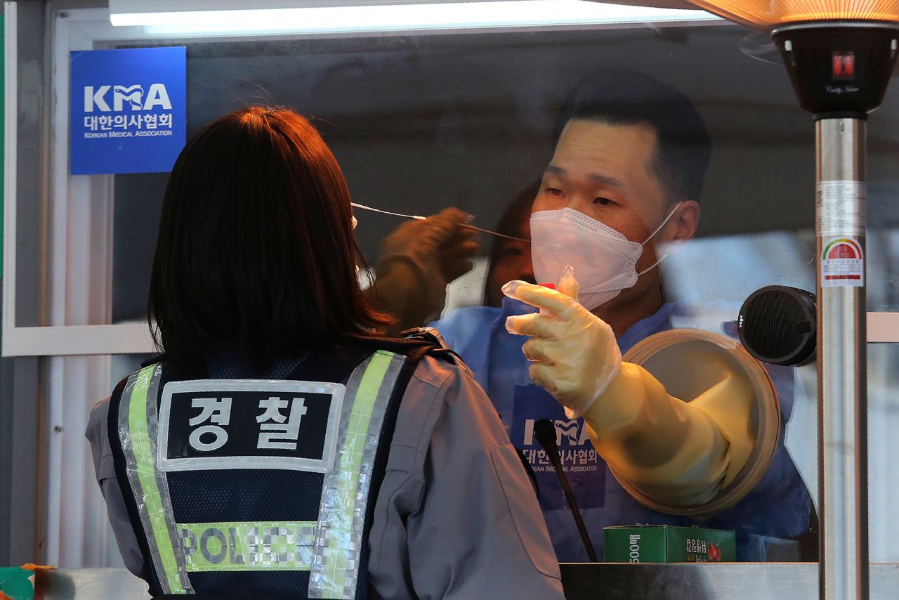 A medical worker in a booth takes nasal samples from a police officer at a coronavirus testing site in Seoul, South Korea, on January 8.