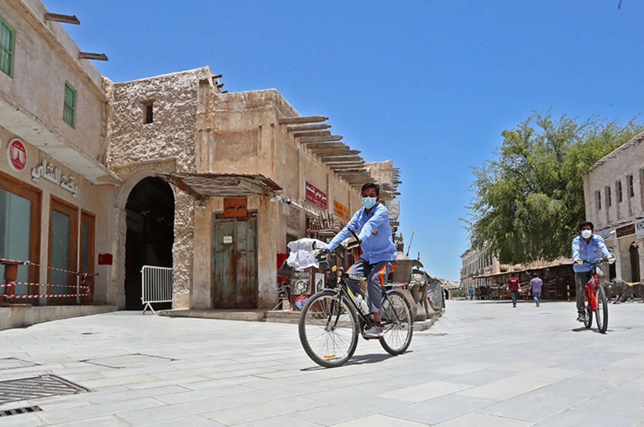 Workers wearing masks ride bicycles at Qatar's touristic Souq Waqif bazar in the capital Doha, on Sunday, May 17, as the country begins enforcing the world's toughest penalties for failing to wear masks.