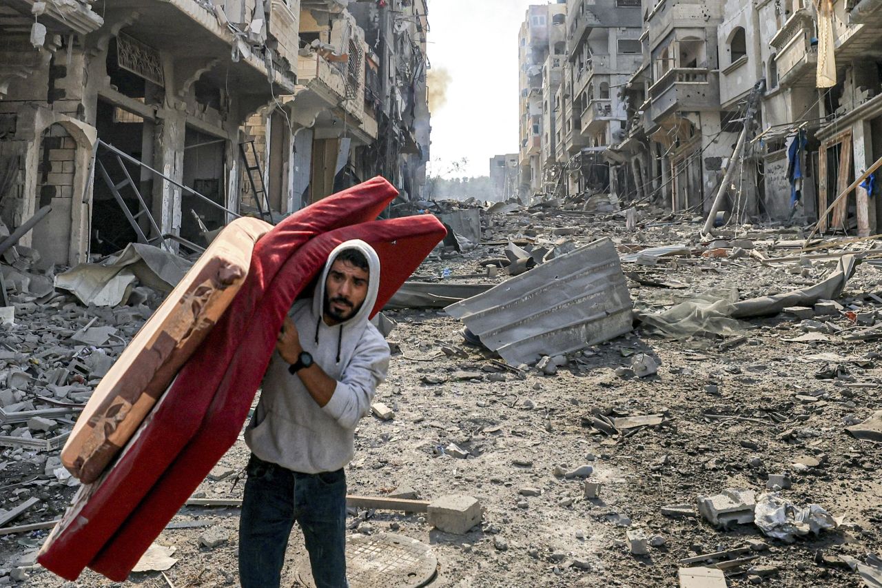 A man walks with mattresses through destruction in Gaza's Jabalia refugee camp on October 11, 2023.