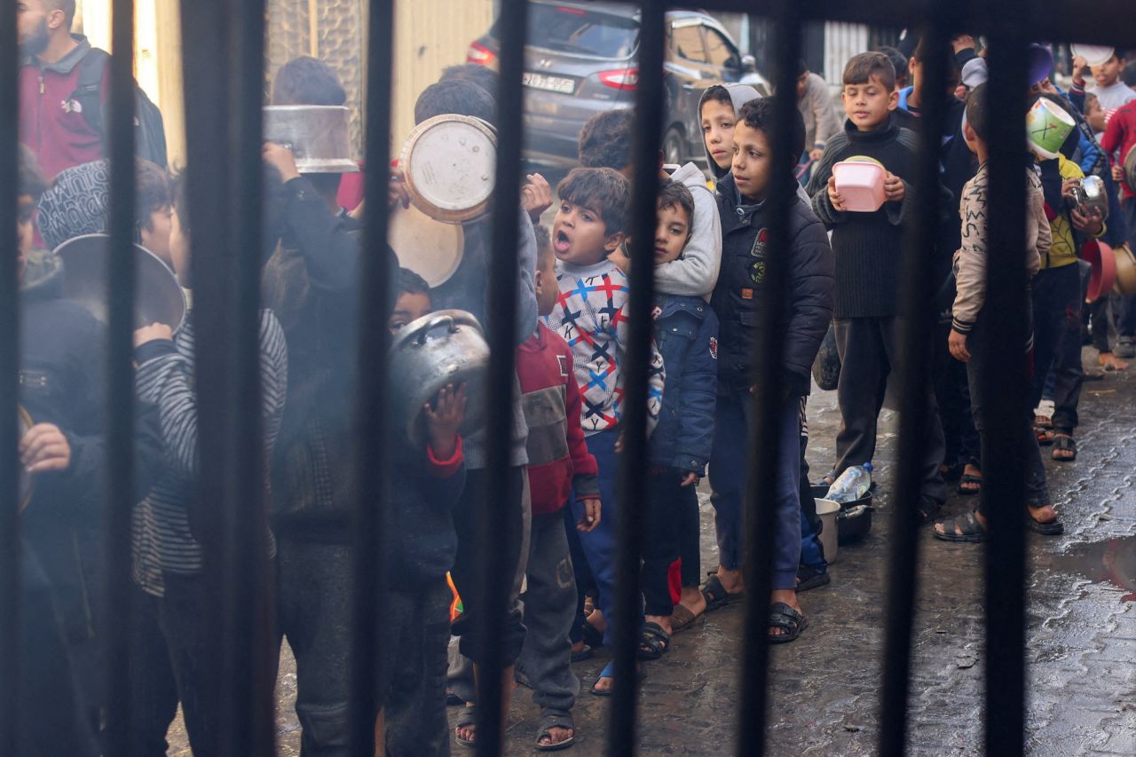 Palestinian children carry pots as they line up to receive food cooked by a charity kitchen in Rafah, Gaza, on December 14.