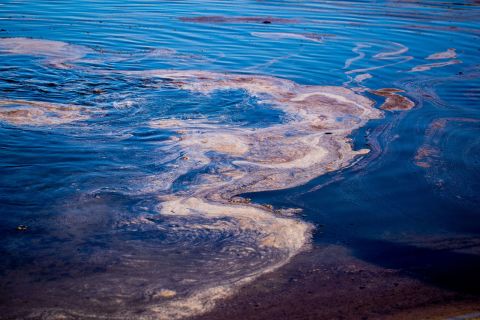 Oil that has formed into globules, foam and sheen is trapped in a sand pool at the Santa Ana River Jetties in Huntington Beach.
