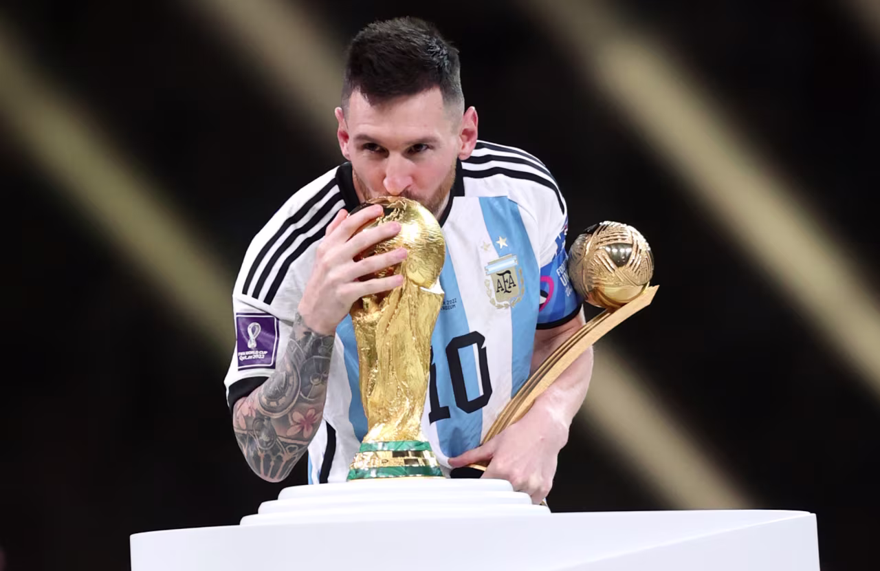 Messi, holding the Golden Ball trophy, kisses the World Cup.