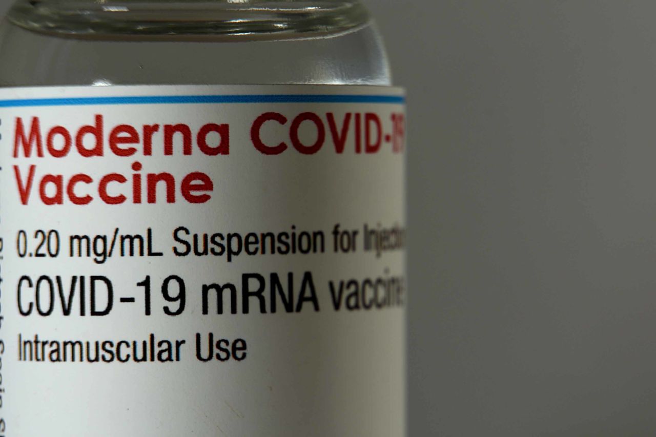 A close-up shows a vial of the Moderna vaccine.