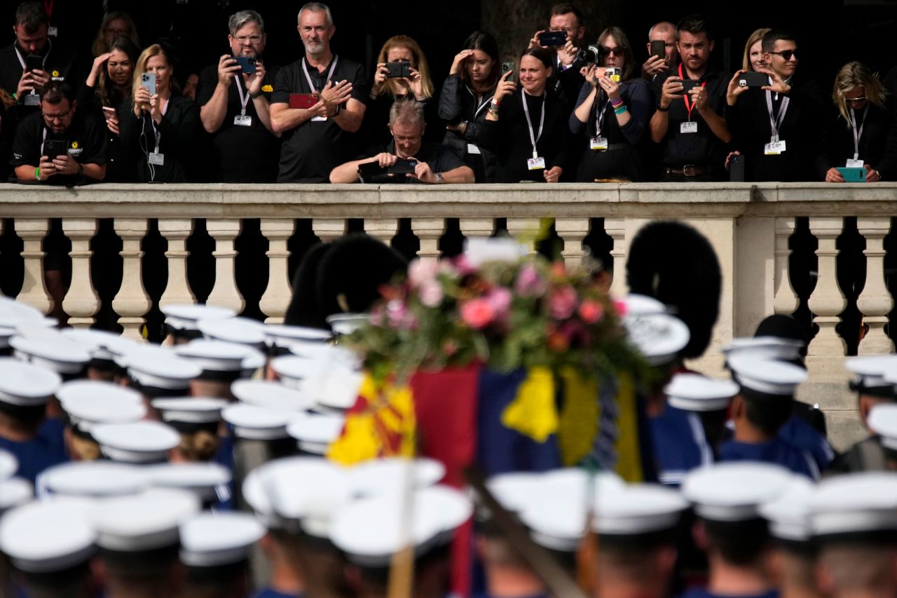 People take pictures of the coffin of the Queen being pulled past Buckingham Palace.