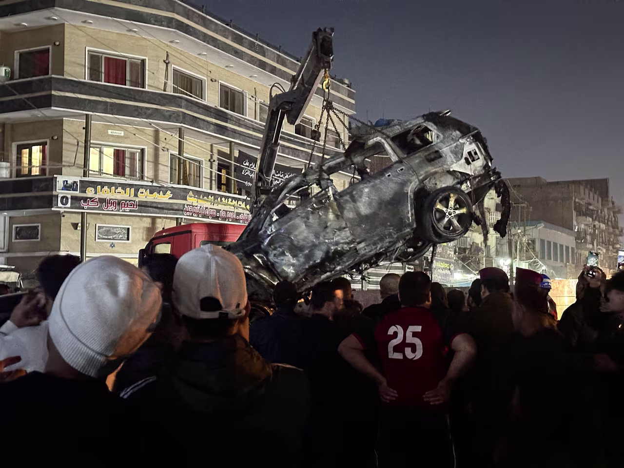 People gather as a destroyed vehicle is loaded onto a truck, after what security sources said was a deadly drone strike, in Baghdad, Iraq, on February 7. 