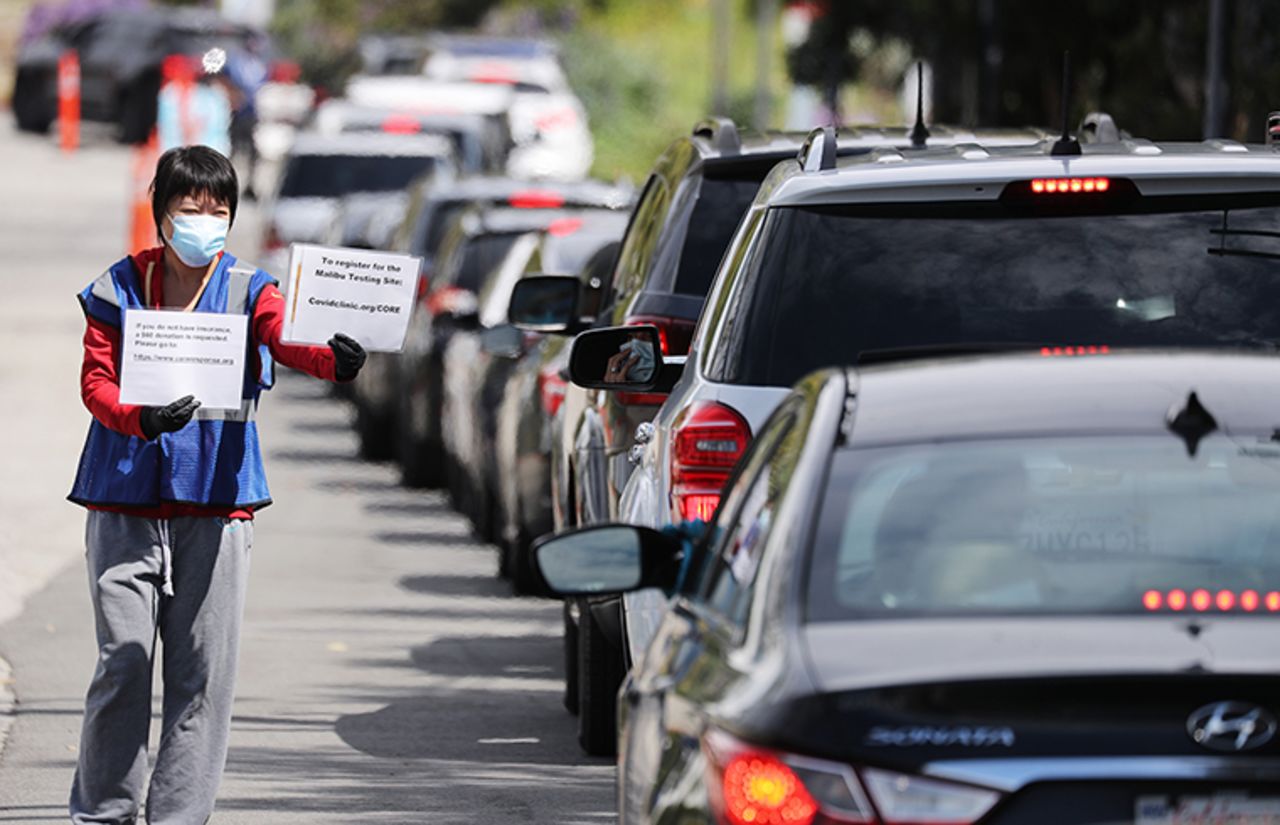 Volunteer Charlotte Xia wears a mask as she shows instructions to drivers during drive-through coronavirus testing at Malibu City Hall on Wednesday, April 8, in Malibu, California. 