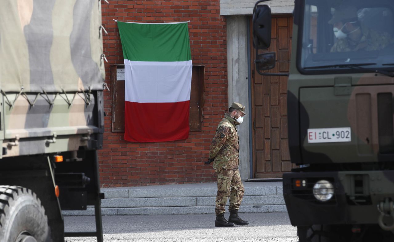 An Italian flag hangs outside the San Giuseppe church in Seriate, Italy, as a soldier waits to load coffins to be taken to crematoriums, on March 28.