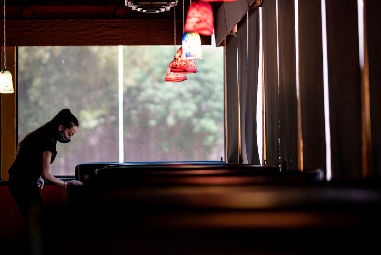 A waitress wearing a mask and gloves disinfects a table in a Restaurant on May 5, in Stillwater, Oklahoma.