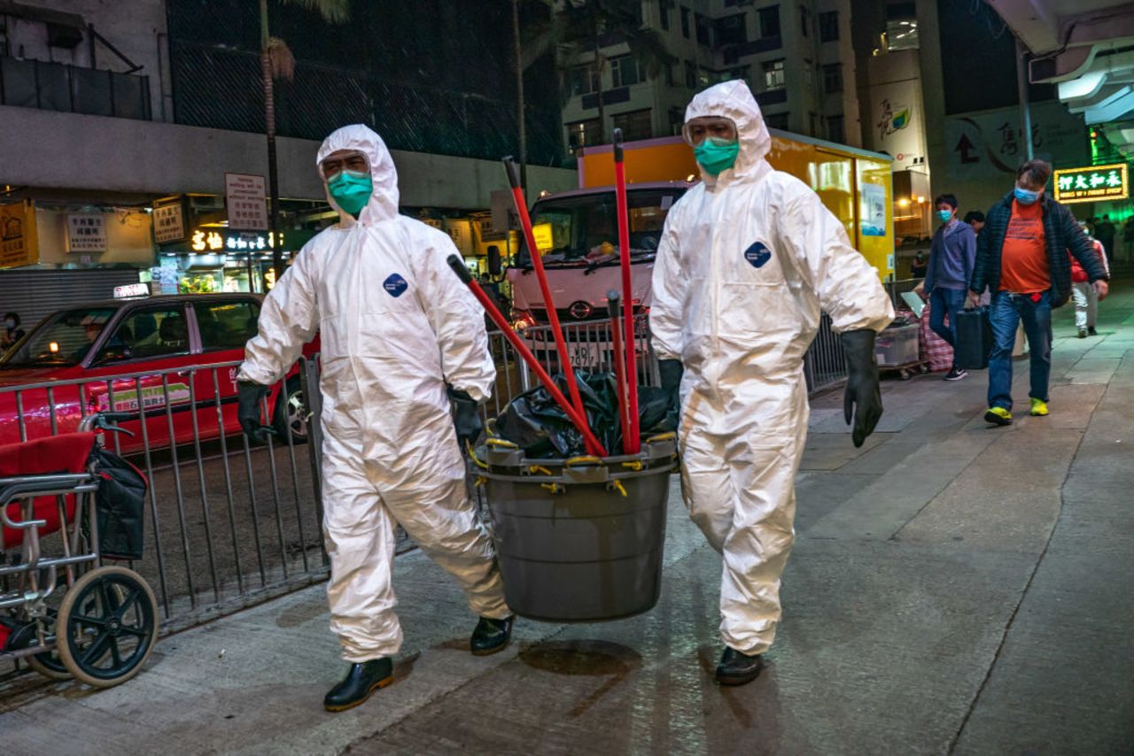 Workers wearing personal equipment carry cleaning supplies into a residential building at North Point district on February 23 in Hong Kong.