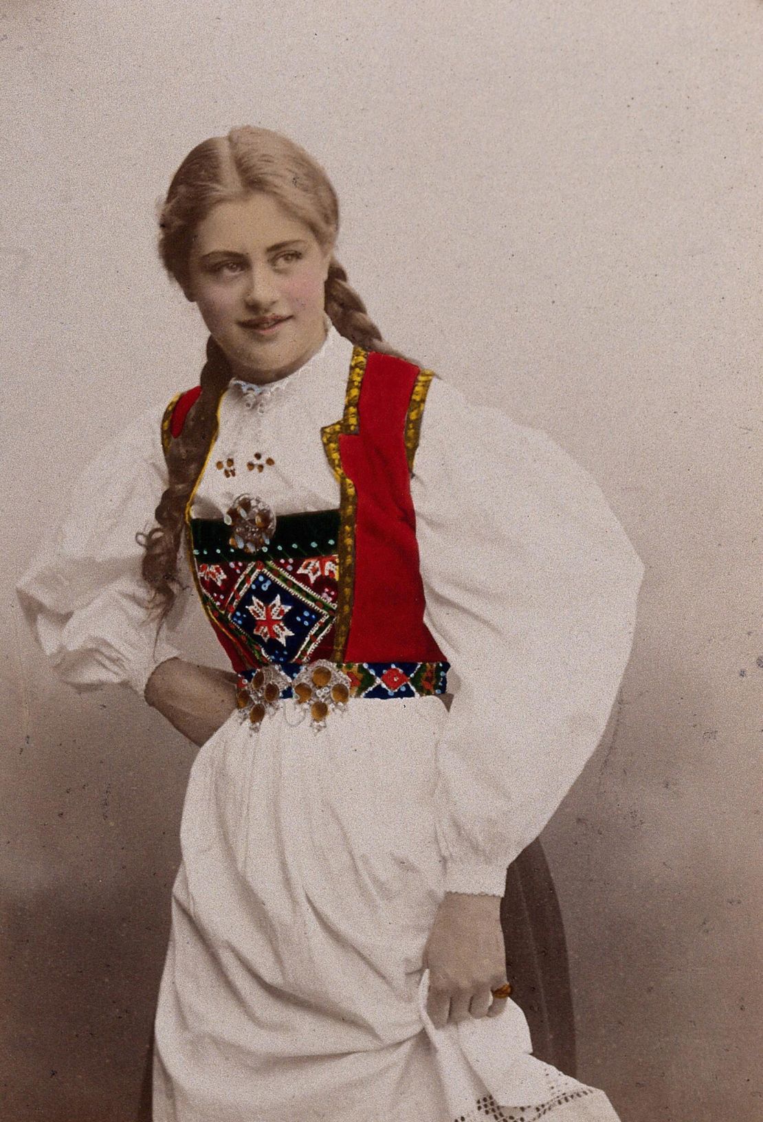 A young Norwegian woman wearing a folk dress poses in a photographic studio in 1901. Traditional Norwegian embroidery might used wool dyed from madder.