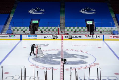 An arena worker removes the net from the ice after the Vancouver Canucks and Calgary Flames NHL hockey game was postponed due to a positive COVID-19 test result, in Vancouver, British Columbia, Wednesday, March 31. 