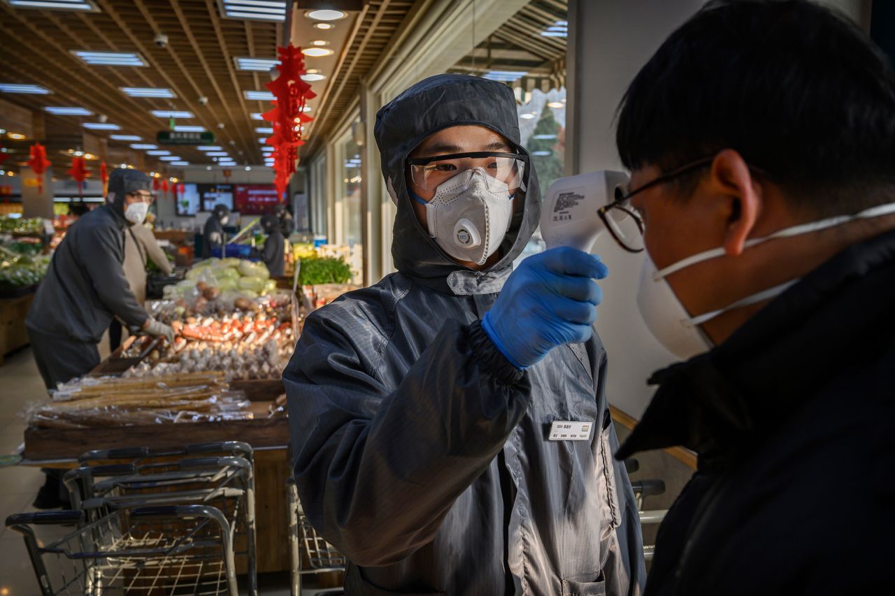 A Chinese worker checks the temperature of a customer as he wears a protective suit and mask at a supermarket on February 11 in Beijing.