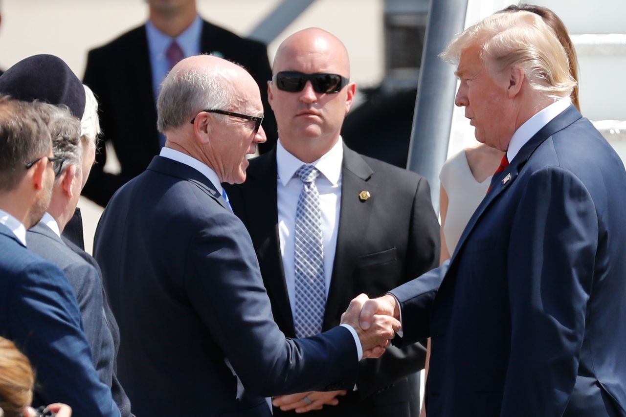 US First Lady Melania Trump (obscured) and US President Donald Trump (R) are greeted by US Ambassador to the United Kingdom Woody Johnson.