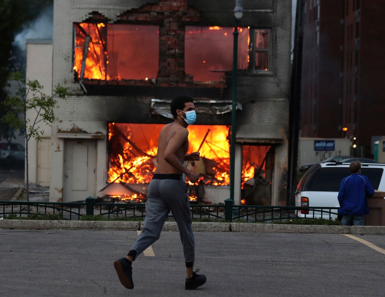 A man runs near a burning building after a night of unrest and protests in the death of George Floyd in downtown Minneapolis, early Thursday, May 28.