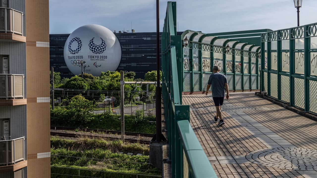 A man passes over a bridge next to a huge semi-sphere bearing the Tokyo Olympics and Paralympics logos on the side of a driving school building on May 6 in Tokyo.?