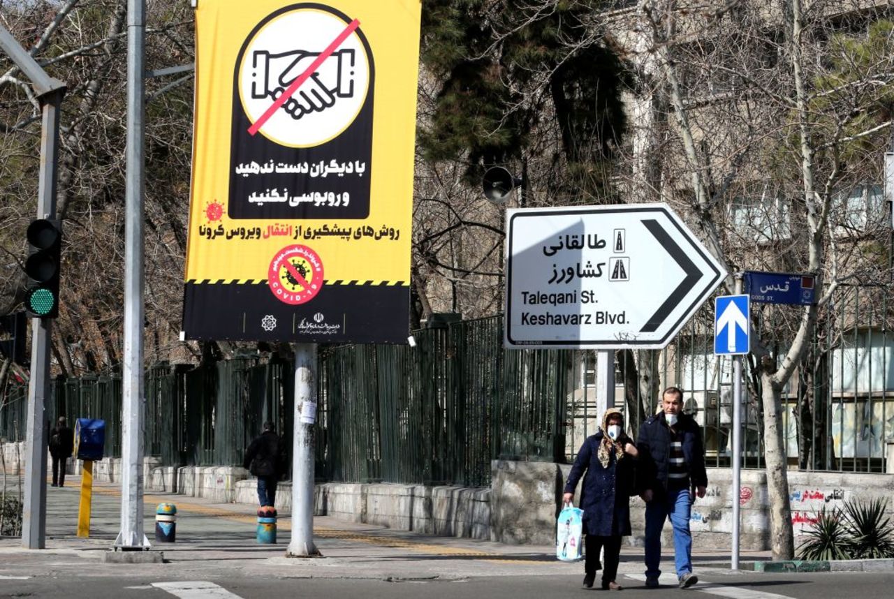 Iranians walk under a coronavirus prevention poster on Wednesday in Tehran, Iran.