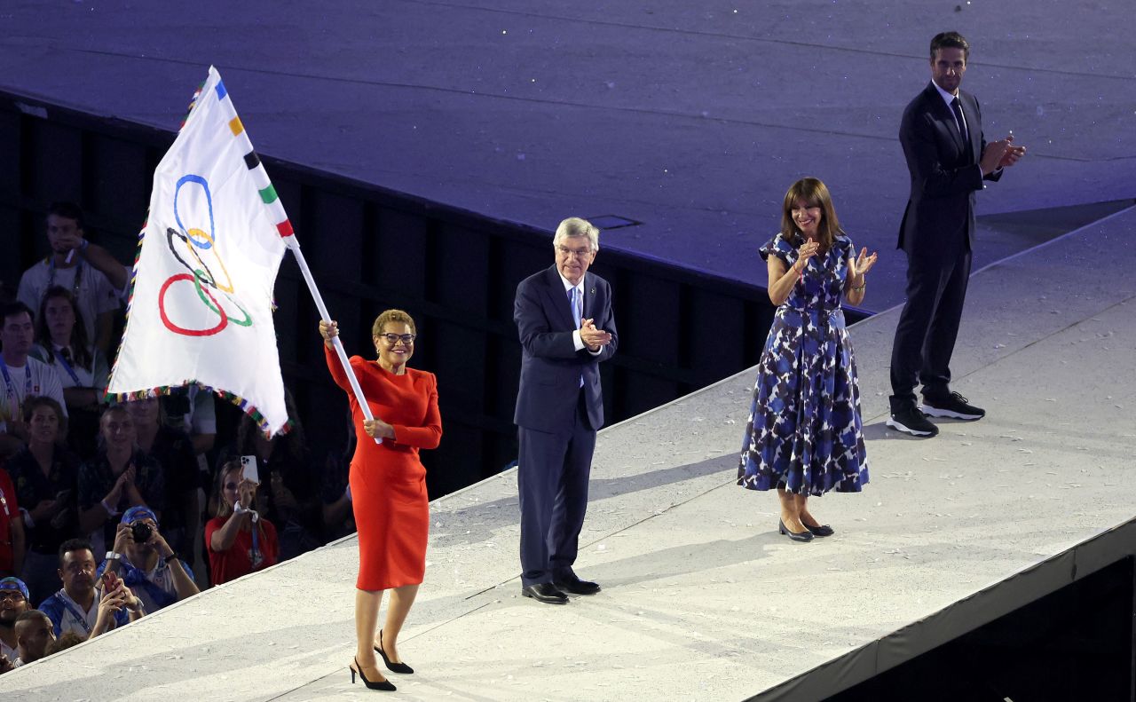 Karen Bass, Mayor of Los Angeles, waves the Olympic flag as Thomas Bach, President of International Olympic Committee, and Anne Hidalgo, Mayor of Paris, applaud. 