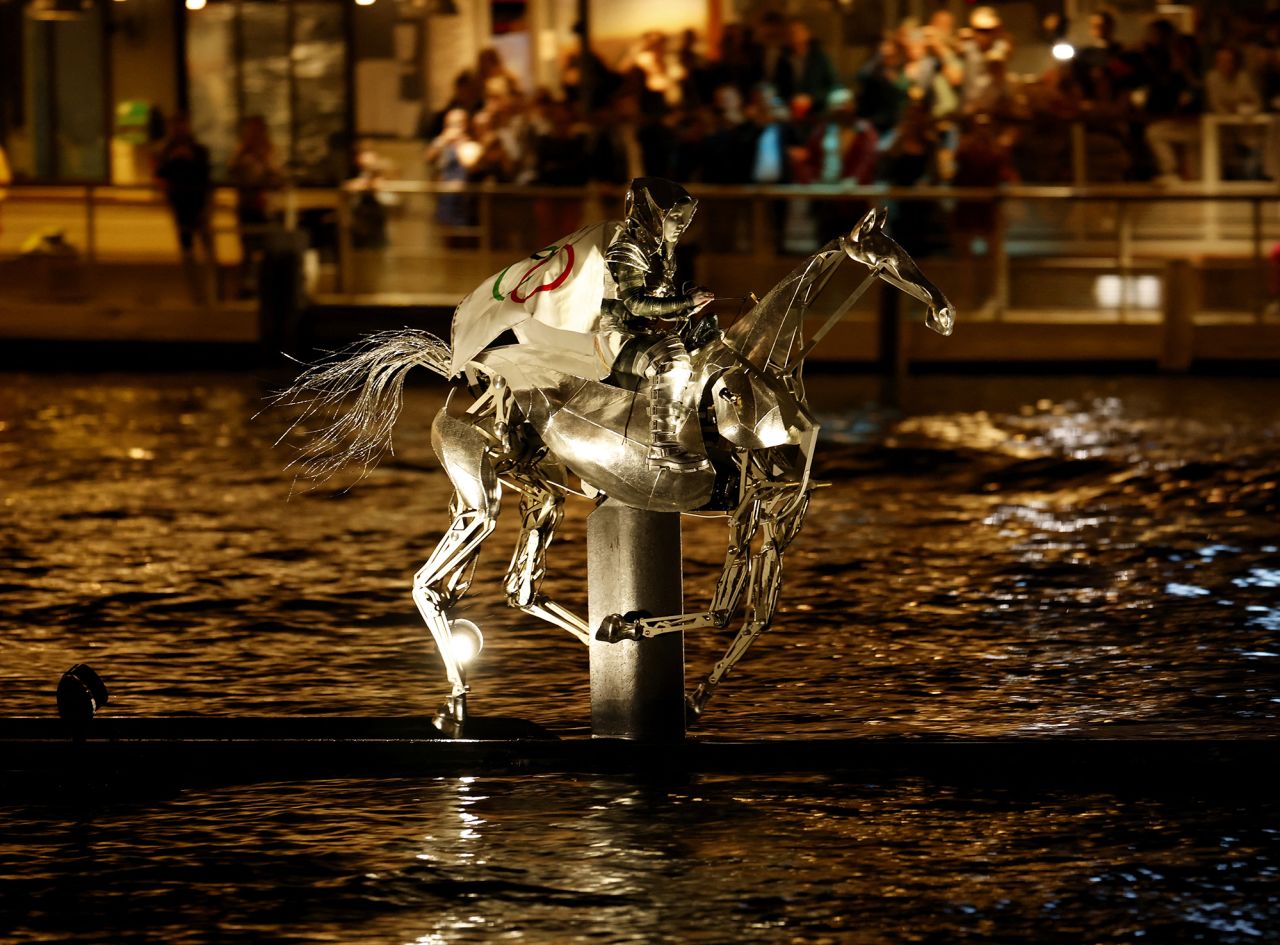 A person on a robotic horse carrying a flag displaying the Olympic rings is seen during the opening ceremony. 