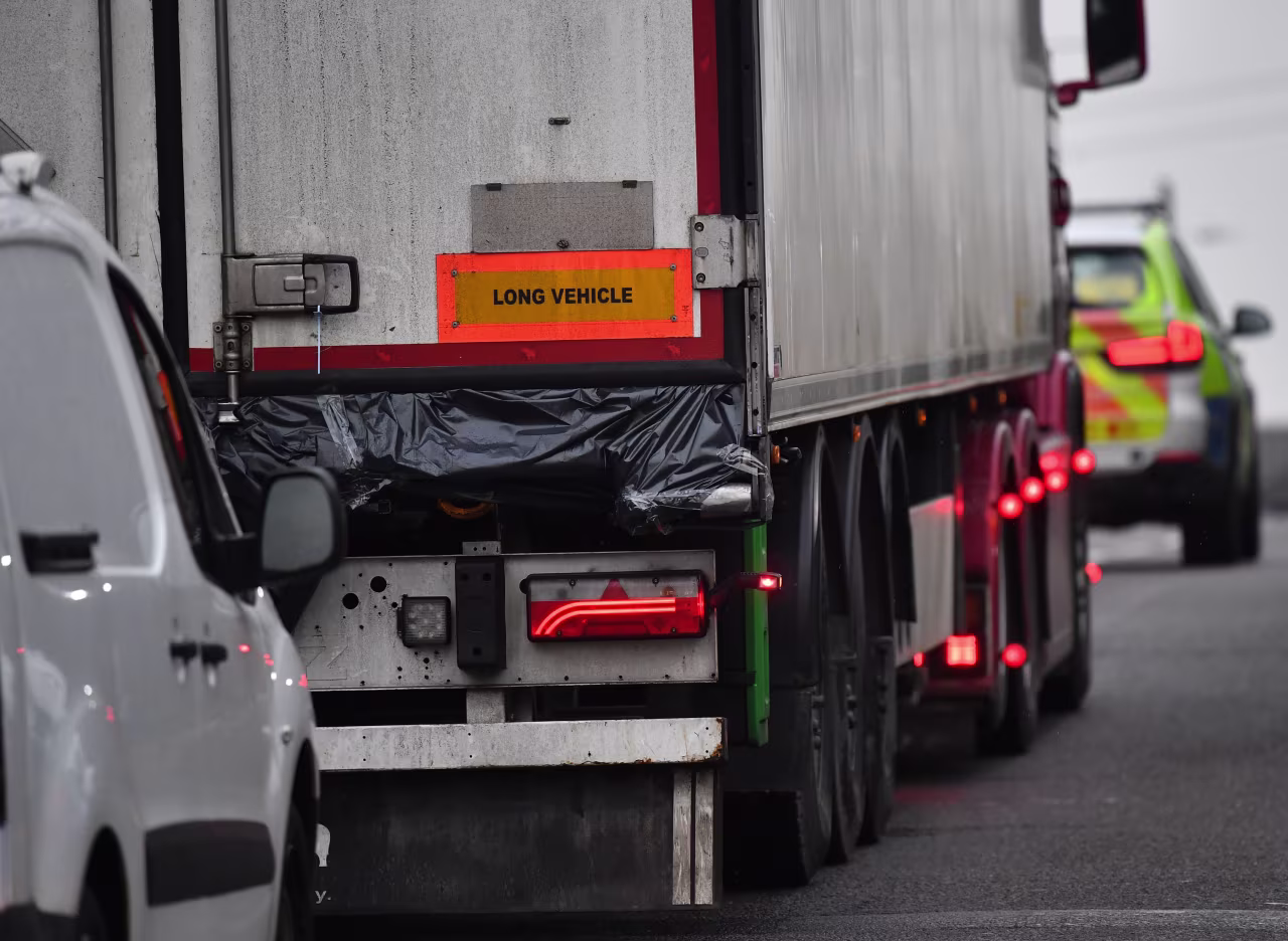 Police officers drive away a lorry, with black plastic visible at the rear, in which 39 bodies were discovered in Essex.