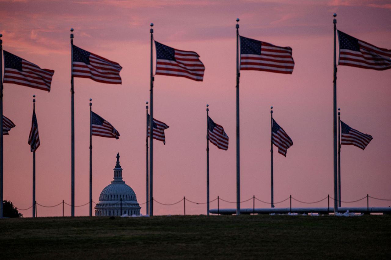 The US Capitol building is seen past flags surrounding the base of the Washington Monument as the sun rises in Washington, DC, on May 28.