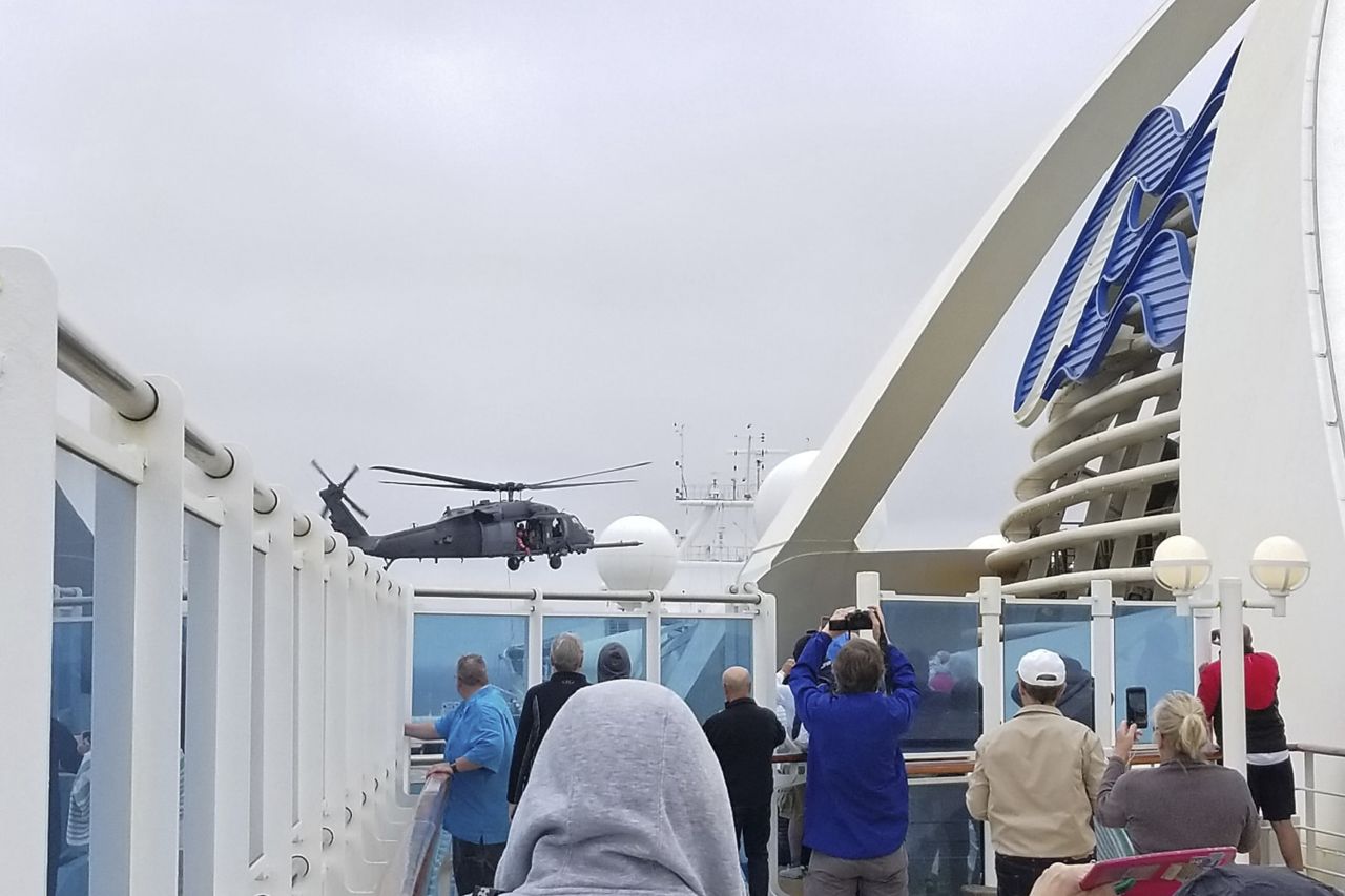 In this photo provided by Michele Smith, passengers look on as a National Guard helicopter hovers above the Grand Princess cruise ship off the California coast on Thursday.