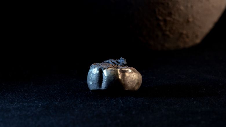 The gold earring found by the scientists, photographed against a dark background, in front of the jar it was found in.