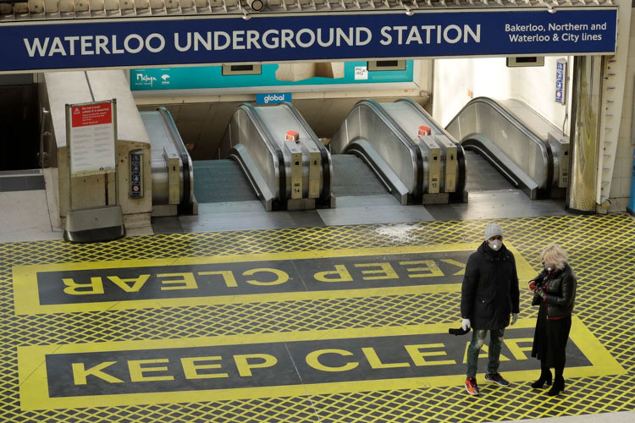 Two people waring masks stand at the top of a bank of escalators in London's Waterloo Station in London on Tuesday, March 24.