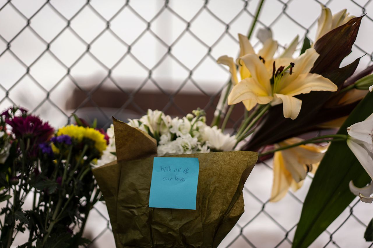 A note left on a bouquet of flowers reads "with all of our love."