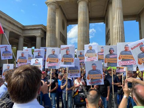 Protesters in Berlin hold up placards featuring pictures of German lawmakers and the word "Guilty." 