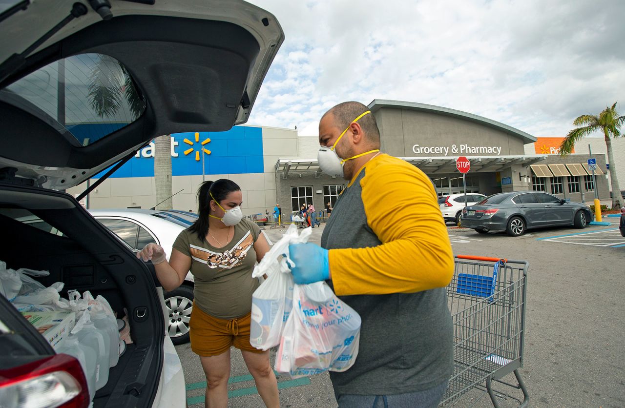 Joel Porro and Lizz Hernandez wear gloves and protective masks as they put bags in the trunk of their car after shopping at Walmart Supercenter in Miami.