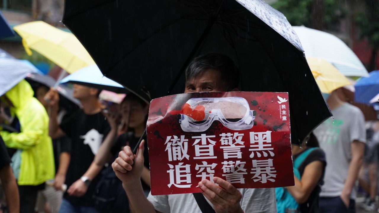 A man holds a sign referencing an incident where a protester was injured in the eye by police. 