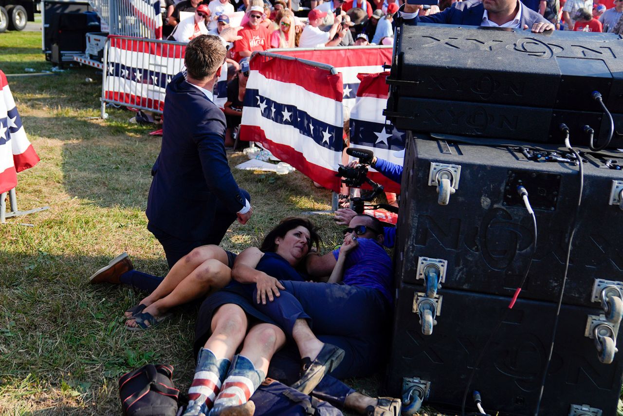 People take cover as Secret Service agents surround Republican presidential candidate former President Donald Trump on stage.