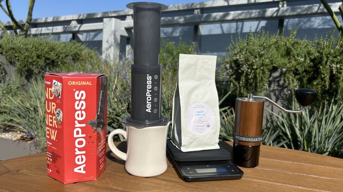 aeropress coffee maker next to bag of coffee beans and a manual grinder