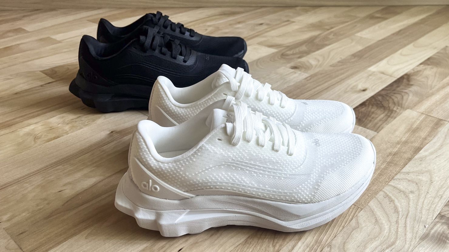 Two pairs of Alo Runner shoes, one in black and one in white.