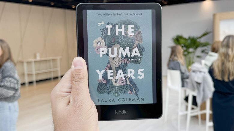 The Amazon Kindle Colorsoft is held aloft and shows the color cover of the book The Puma Years by Laura Coleman