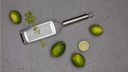 Professional grater on grey countertop surrounded by five limes, one slightly grated.